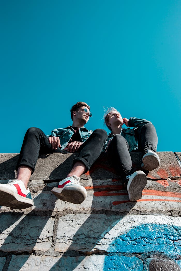 services-01 Two young people sitting on a stone wall under a vibrant blue sky, enjoying a sunny day together.
